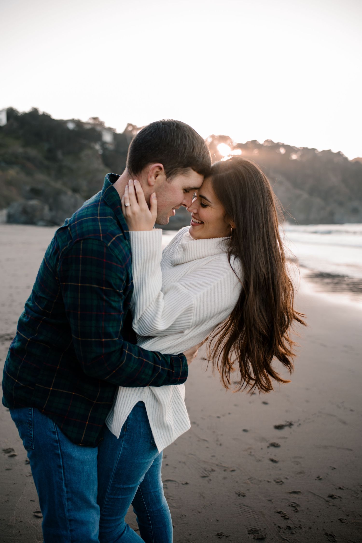 A tender moment between a couple on a misty beach during golden hour.