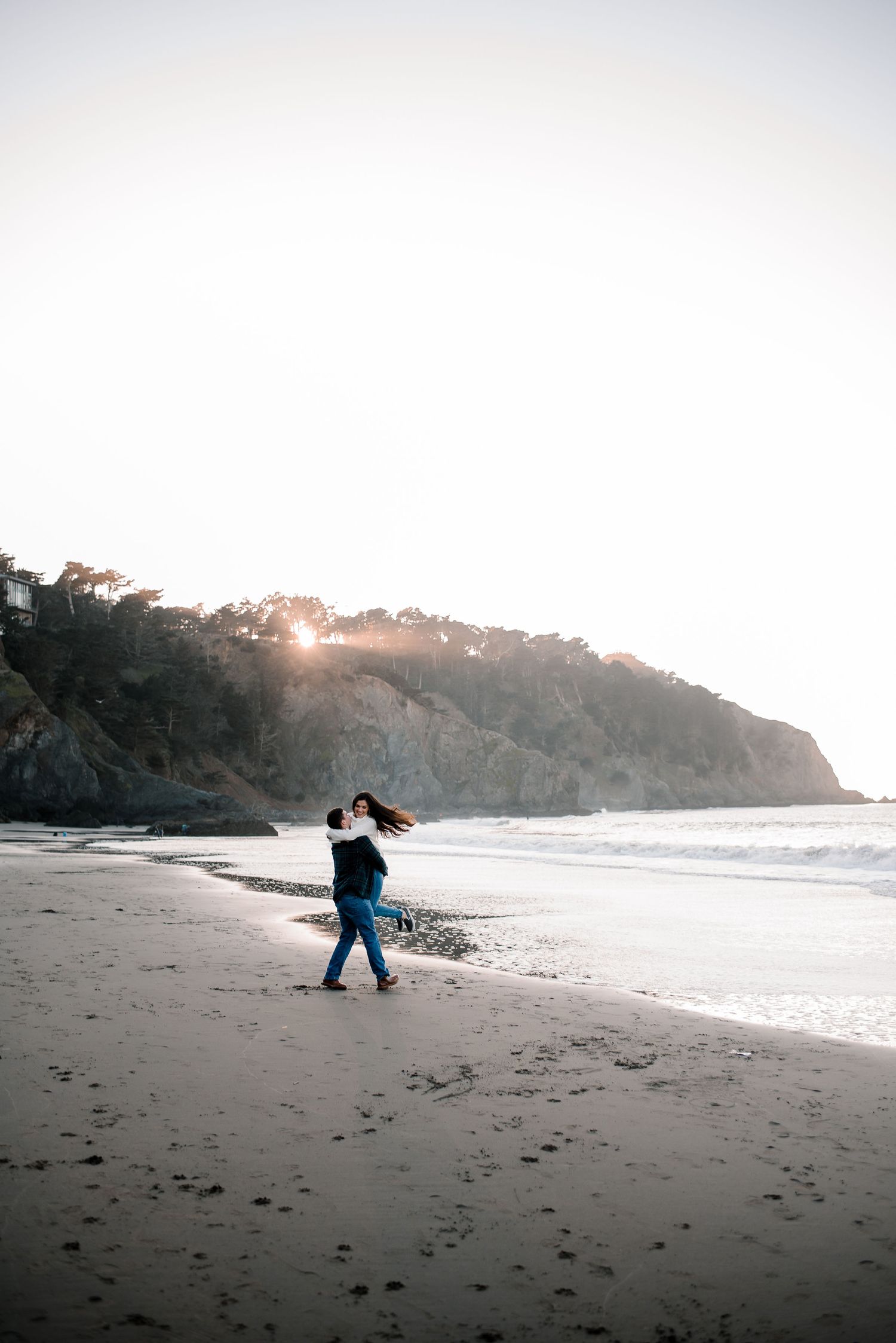 A wide angle shot of a couple walking along a misty California beach at sunset.