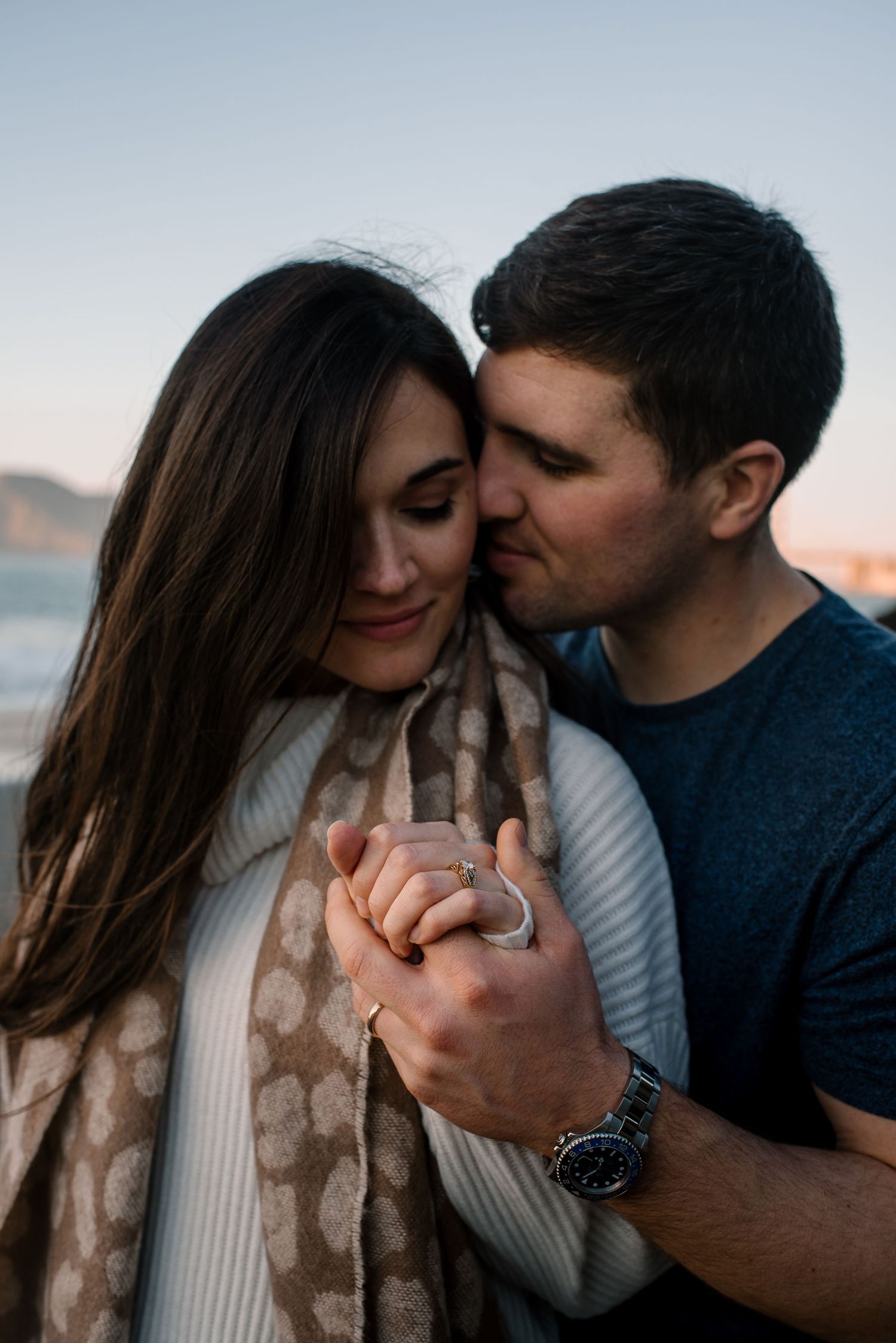 An intimate moment captured between a couple wearing casual clothing on a cloudy beach.