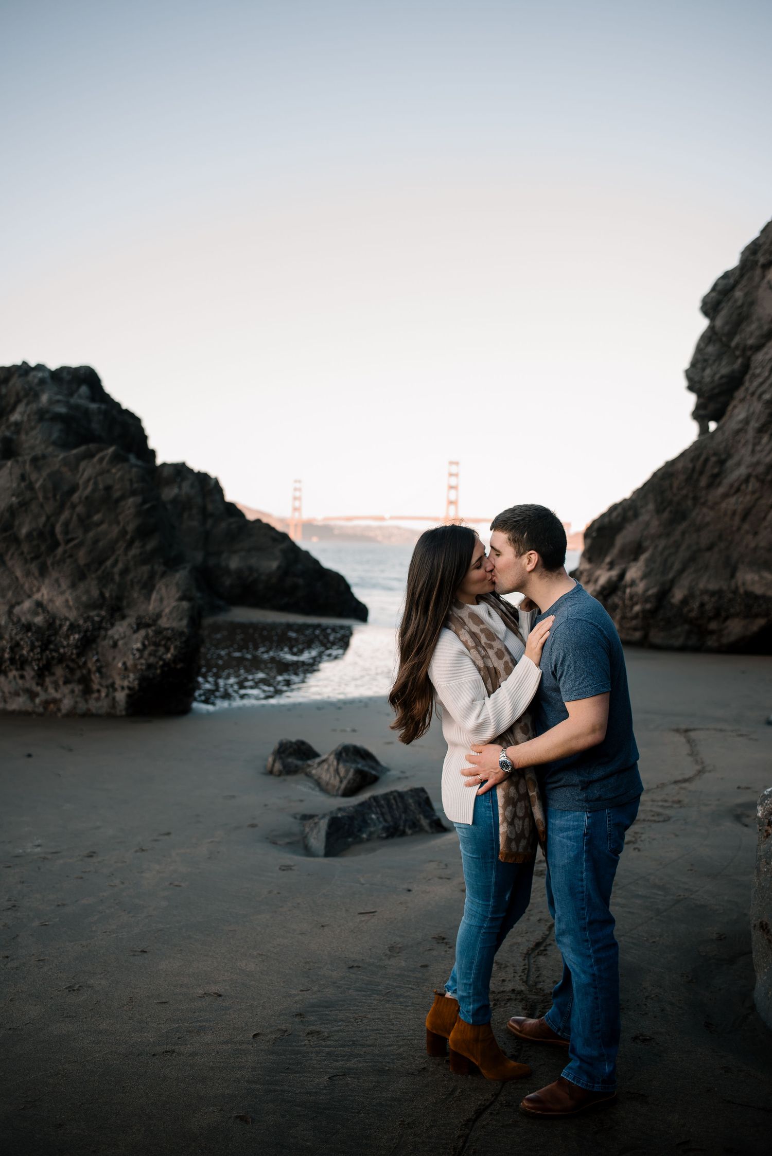 A romantic beach photoshoot featuring a couple embracing near coastal rock formations.