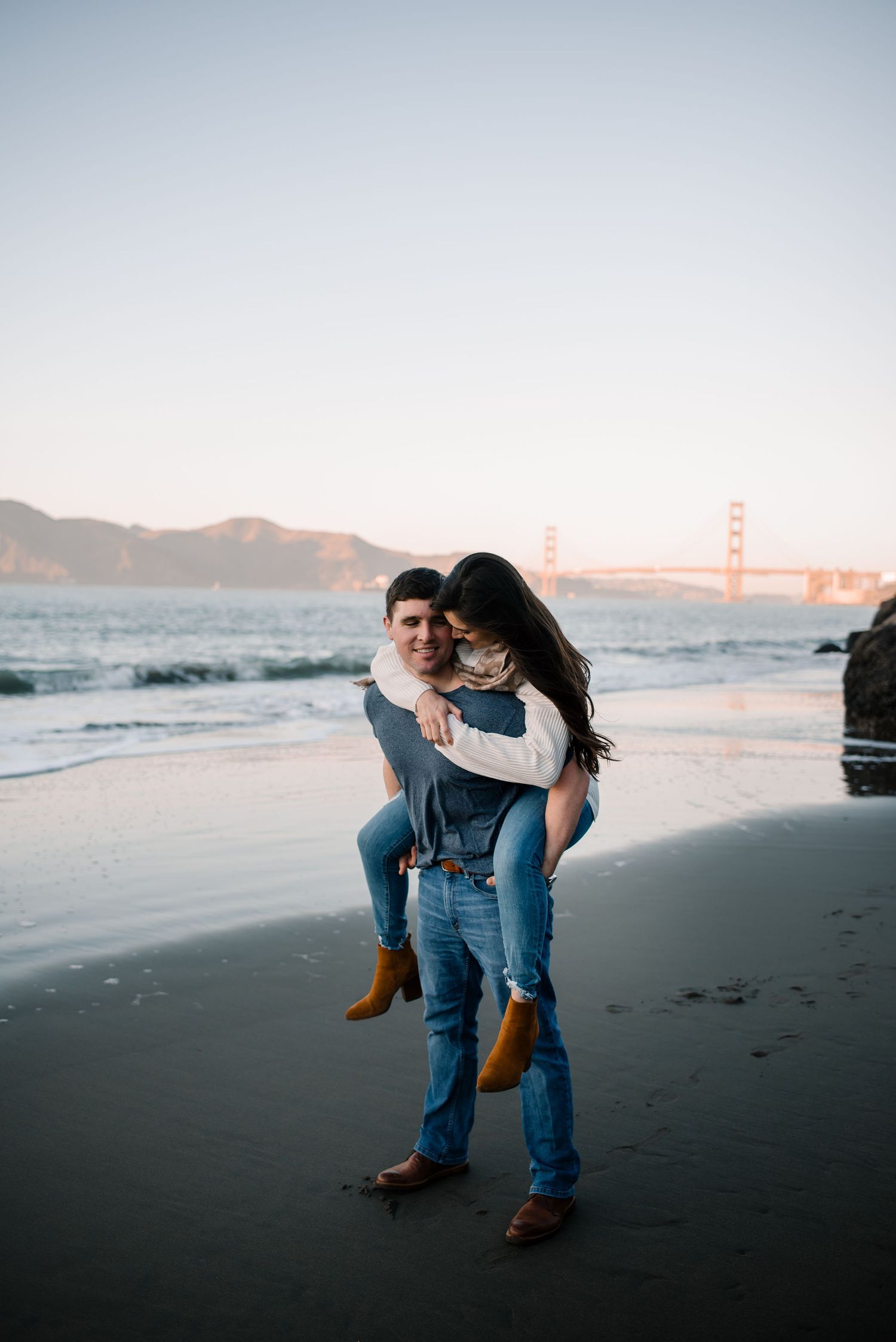 A couple shares a romantic moment on a black sand beach with mountains in the background.