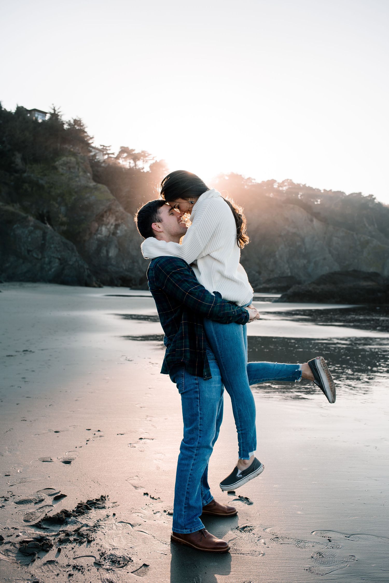 A playful couple interacts on a misty beach at sunset.