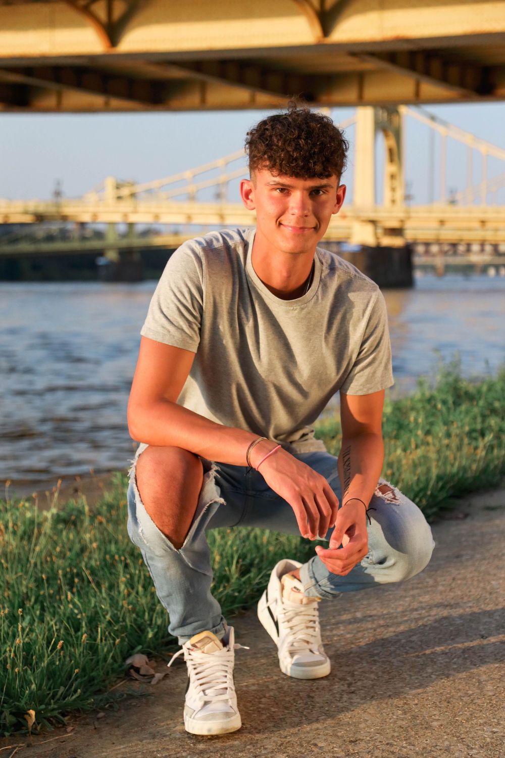 Senior boy poses in golden hour with Pittsburgh bridges in background