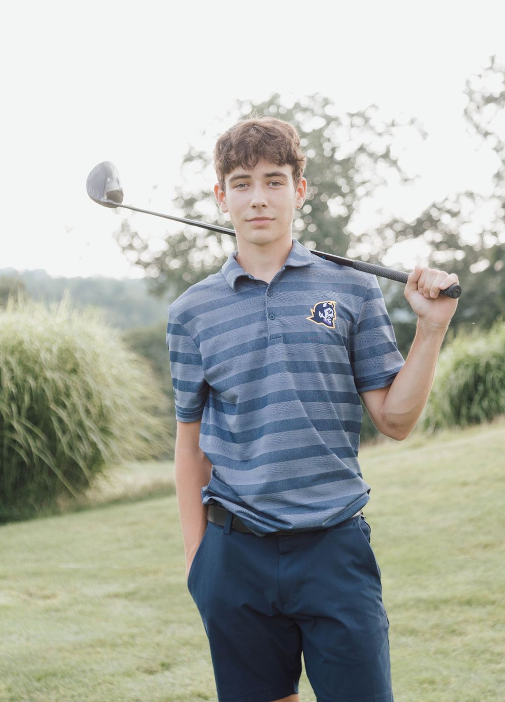 High school senior boy posing with golf club outdoors