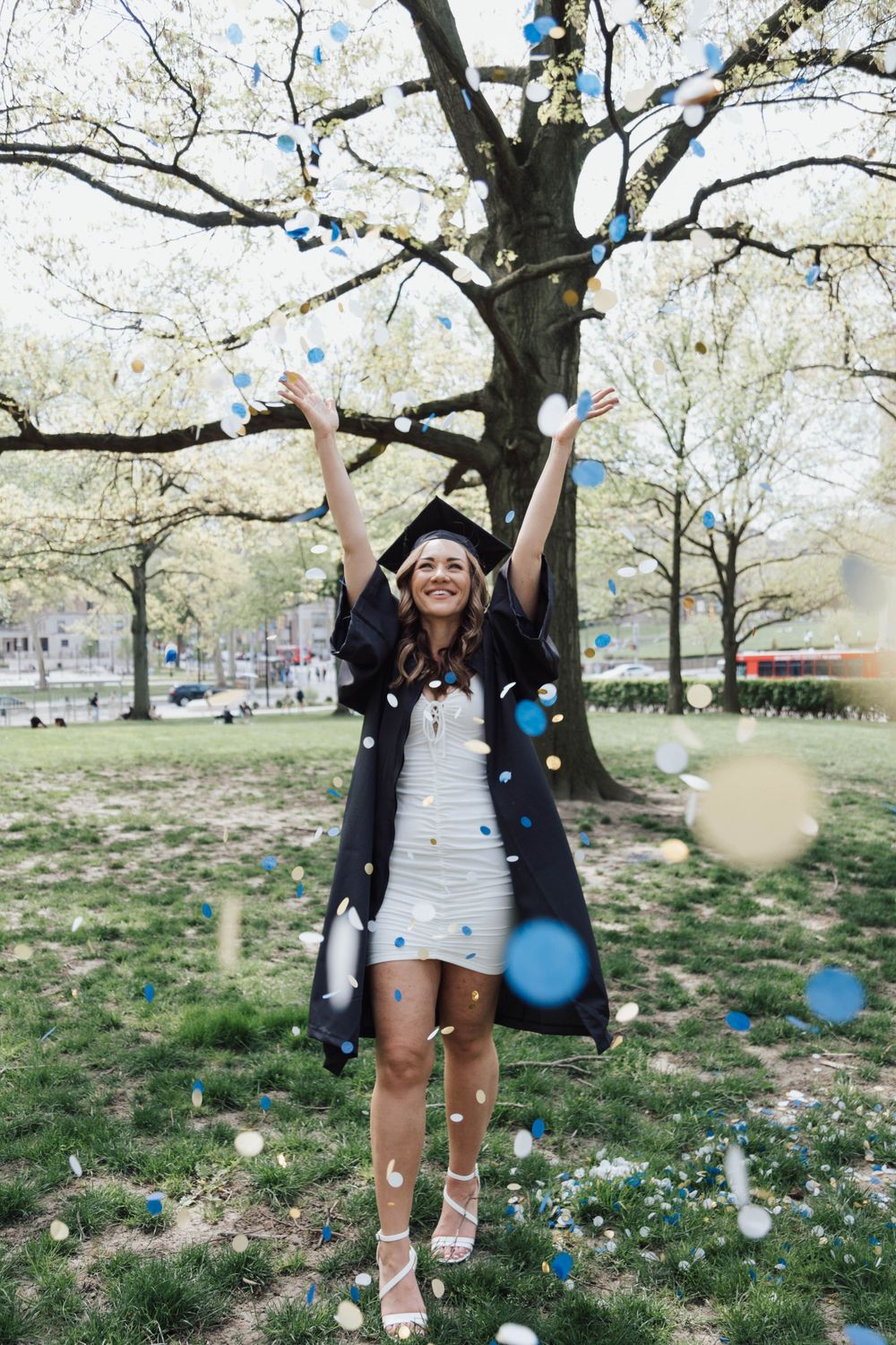 High school senior girl joyfully throwing colorful confetti outdoors
