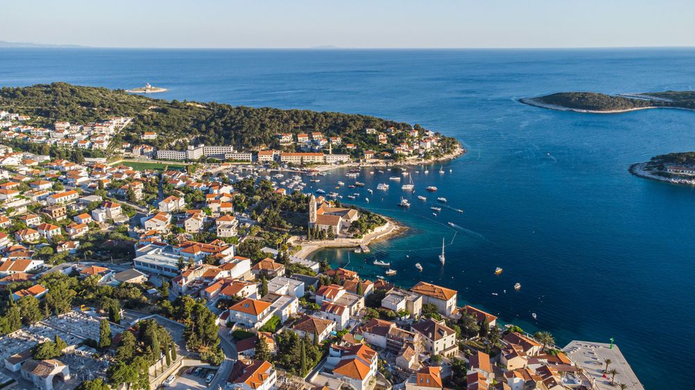 Aerial view of Croatian coastal town with red roofs and boats dotting the blue Adriatic harbor.