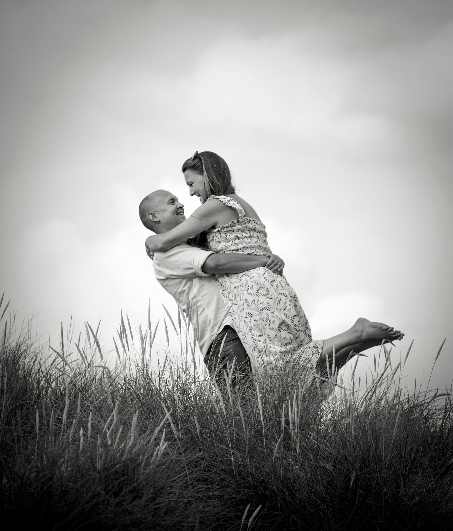 A black and white portrait of two people embracing in tall grass.