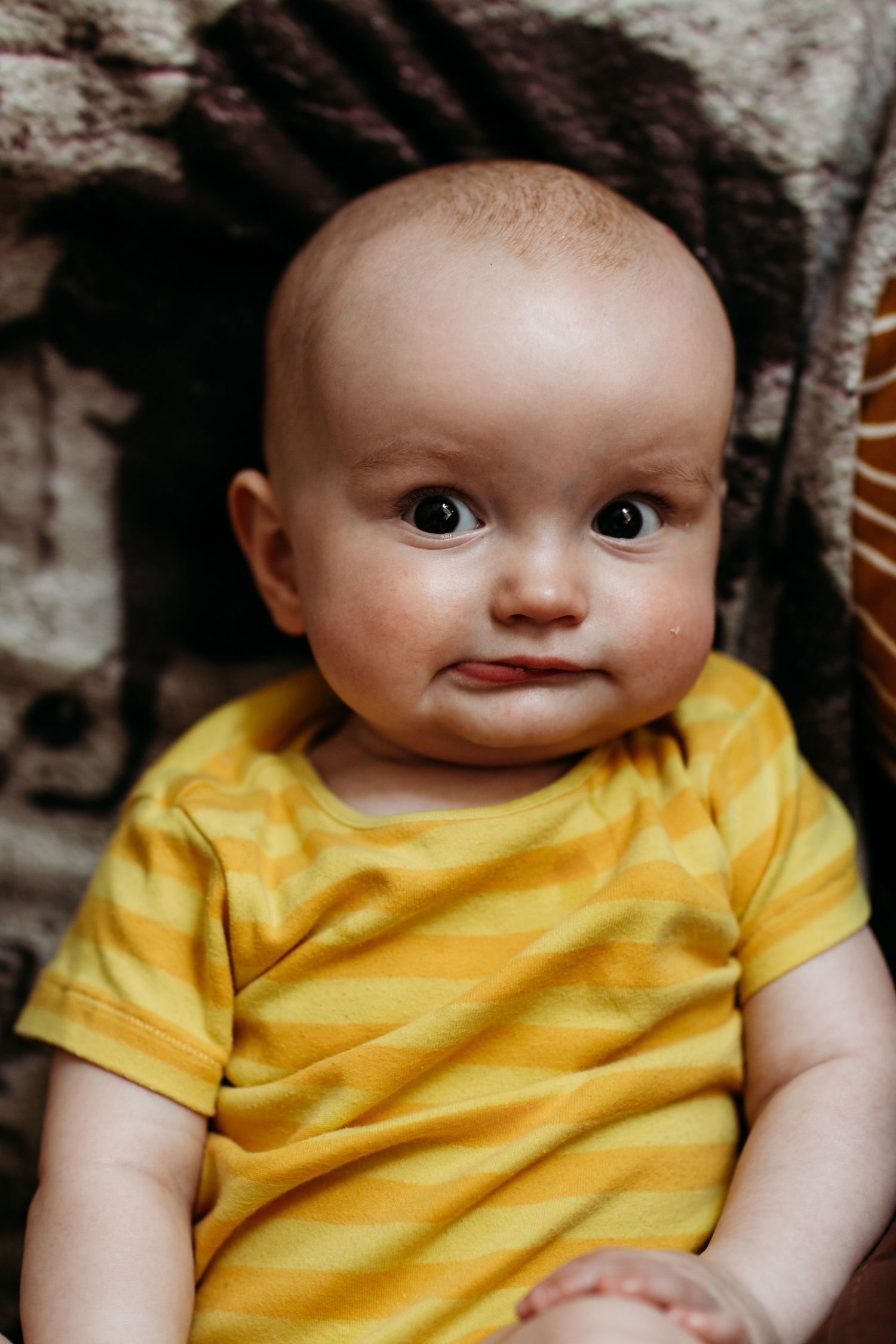 Close-up portrait of an infant in yellow striped shirt against textured background.