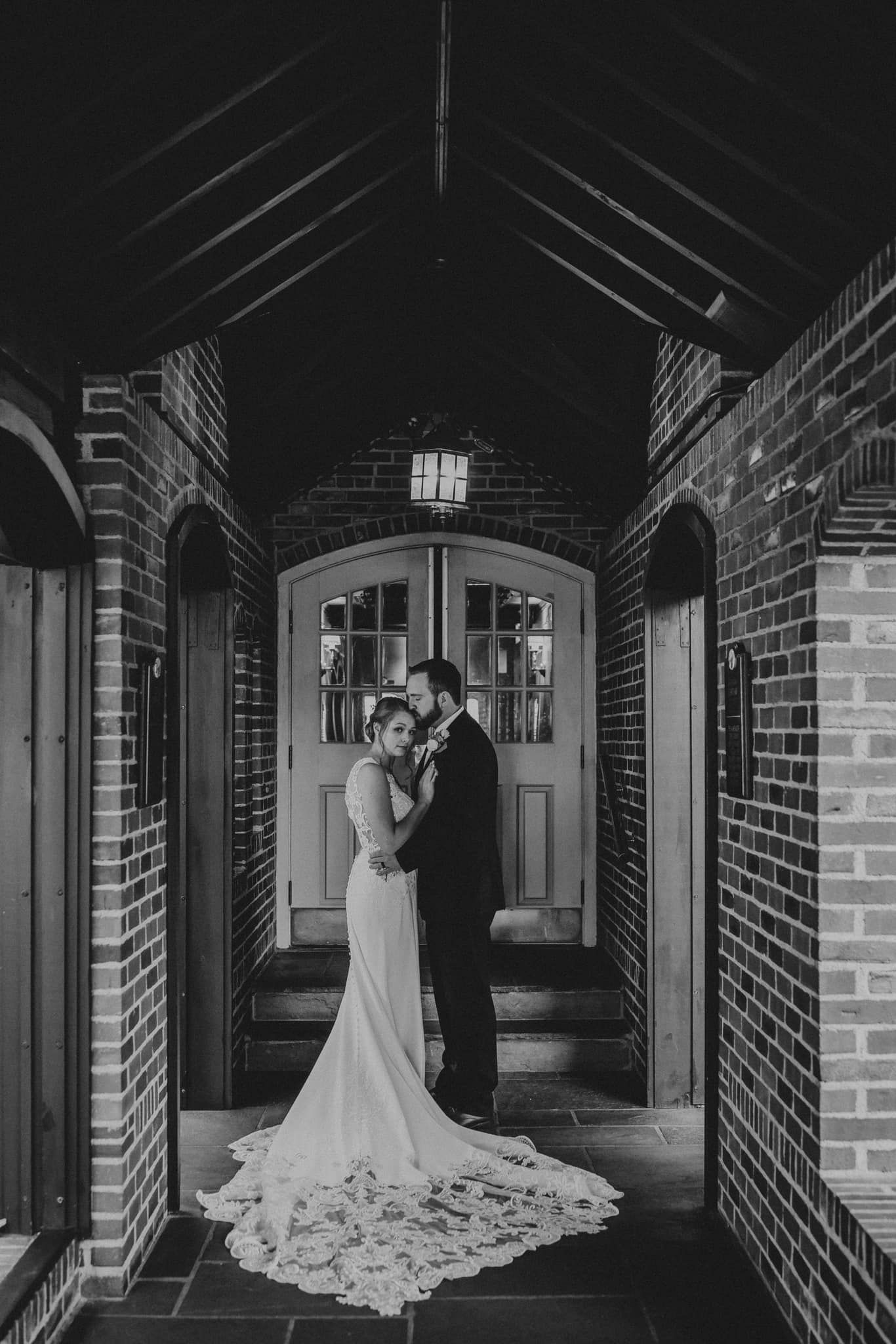 A romantic moment captured in a brick-lined hallway with dramatic lighting and architectural details.