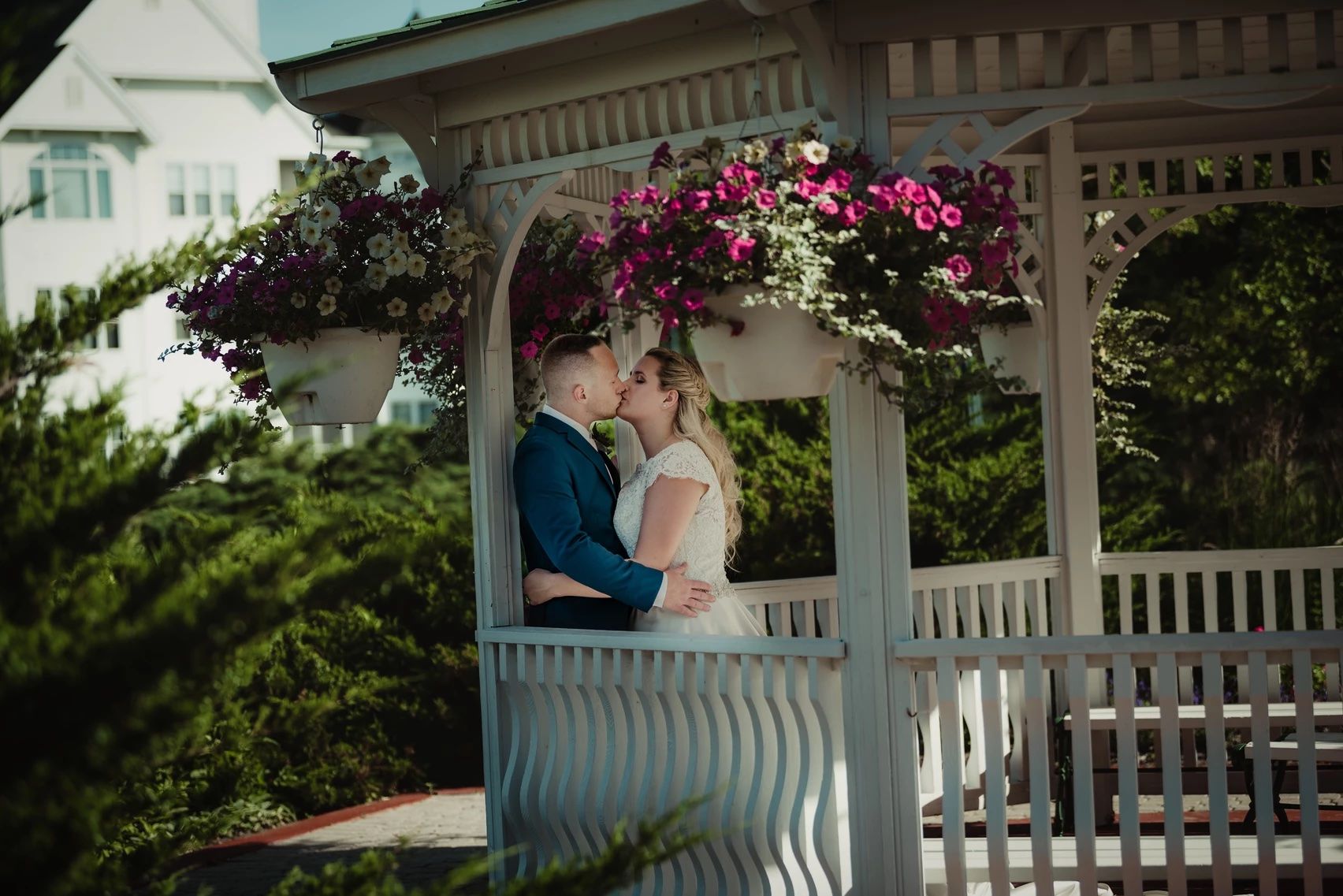 Wedding couple shares an intimate moment under a decorative white gazebo with flowering vines.