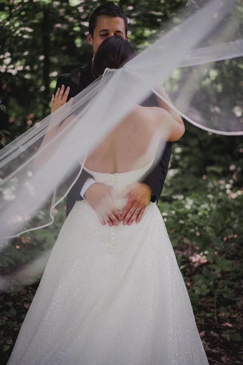 Flowing white wedding dress details shown in an ethereal forest setting with natural light.