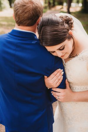An emotional moment between a bride in lace and groom in navy blue during their wedding.