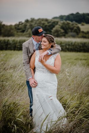 Romantic couple embracing in tall grass field during wedding photoshoot.