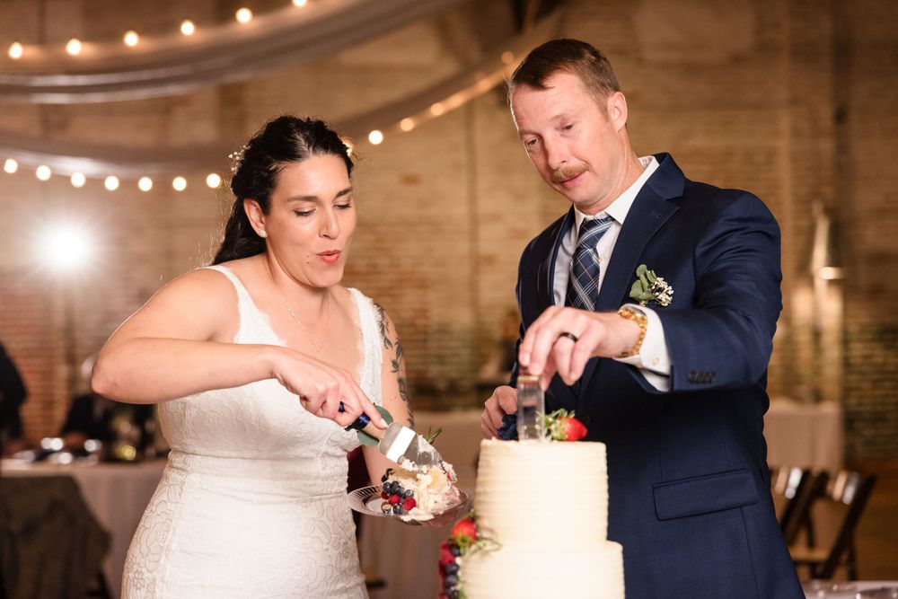 Newlyweds cut their wedding cake together under string lights at reception.