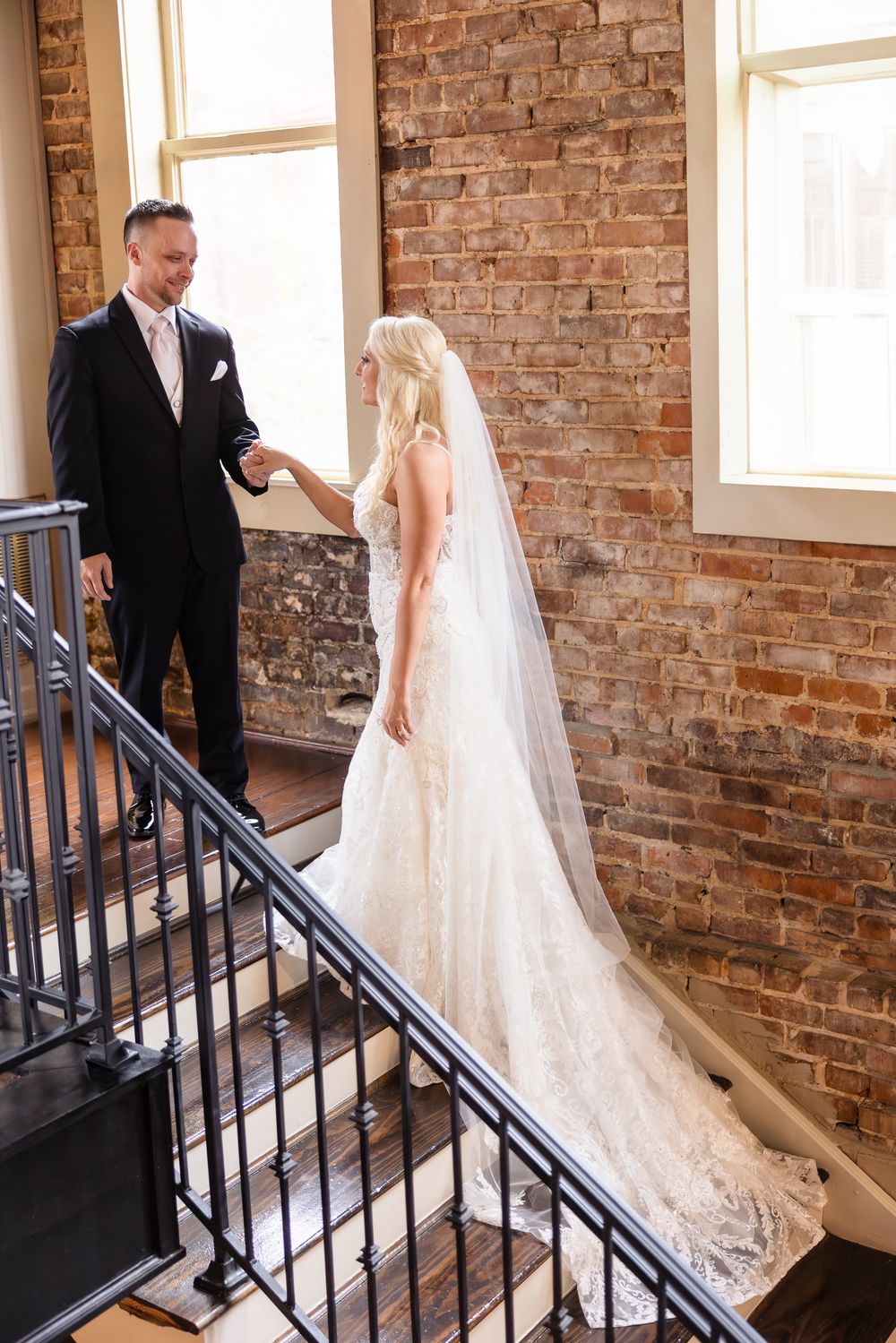 A wedding couple poses on a staircase with exposed brick walls and natural lighting.