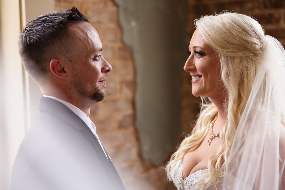 A romantic wedding couple shares intimate moments in a rustic brick venue with natural lighting.