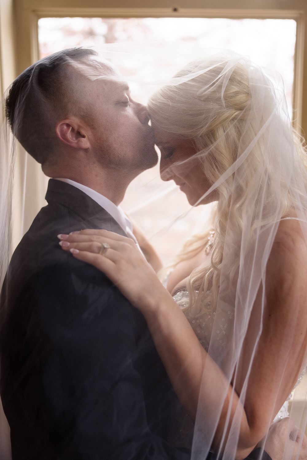 Tender moments between newlyweds as the bride's veil flows in a sunlit indoor setting.