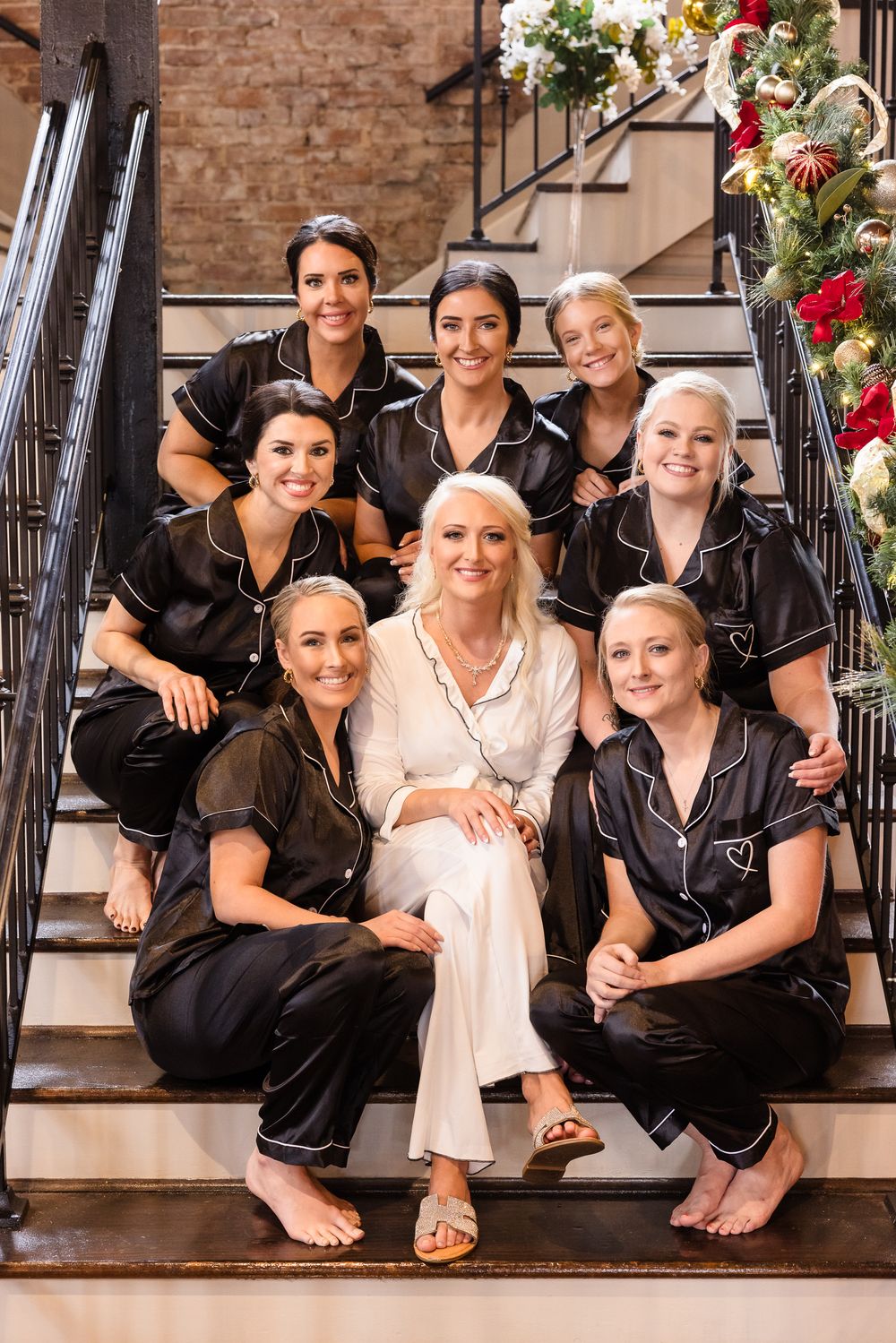 Wedding party in matching black silk pajamas posing on elegant stone staircase.