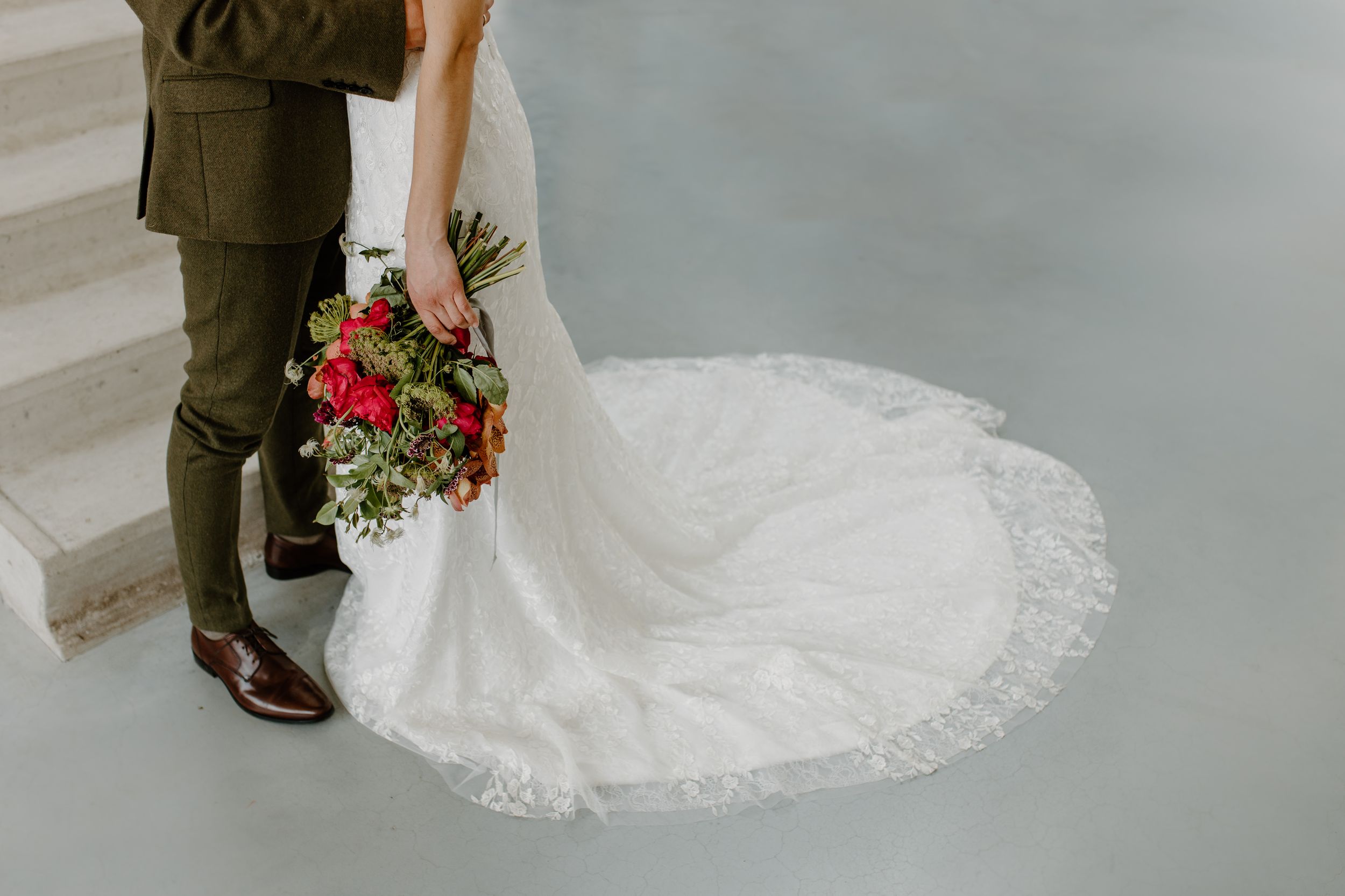 A flowing white wedding dress with lace details and a long train photographed in a minimalist setting.