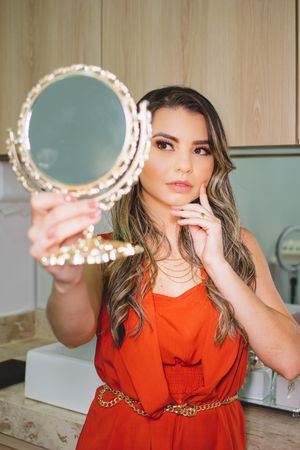 Person in red dress holding decorative mirror while posing for beauty shot.
