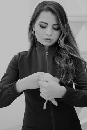 Black and white portrait showing a woman in dark jacket with long wavy hair looking downward pensively.