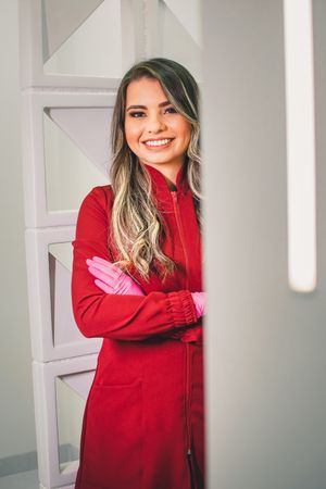 Professional wearing red coat and pink gloves poses confidently against geometric white wall.