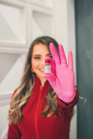 Hand in pink glove holding small medical vial against white modern background.