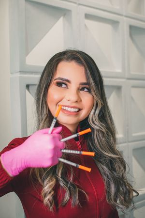 Healthcare worker in red displaying medical supplies with bright smile and pink protective gloves.