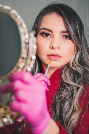 Medical professional applying cosmetic treatment while wearing pink gloves near decorative mirror.