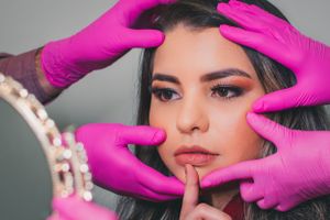 Artistic beauty portrait with pink gloved hands framing face against mirror background.