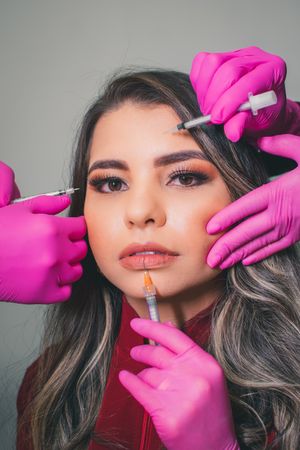 Professional cosmetic treatment being performed with pink gloved hands applying product to client wearing red.