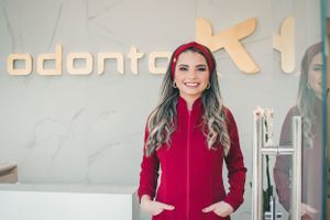 Dental professional in red uniform standing in modern office with illuminated signage.