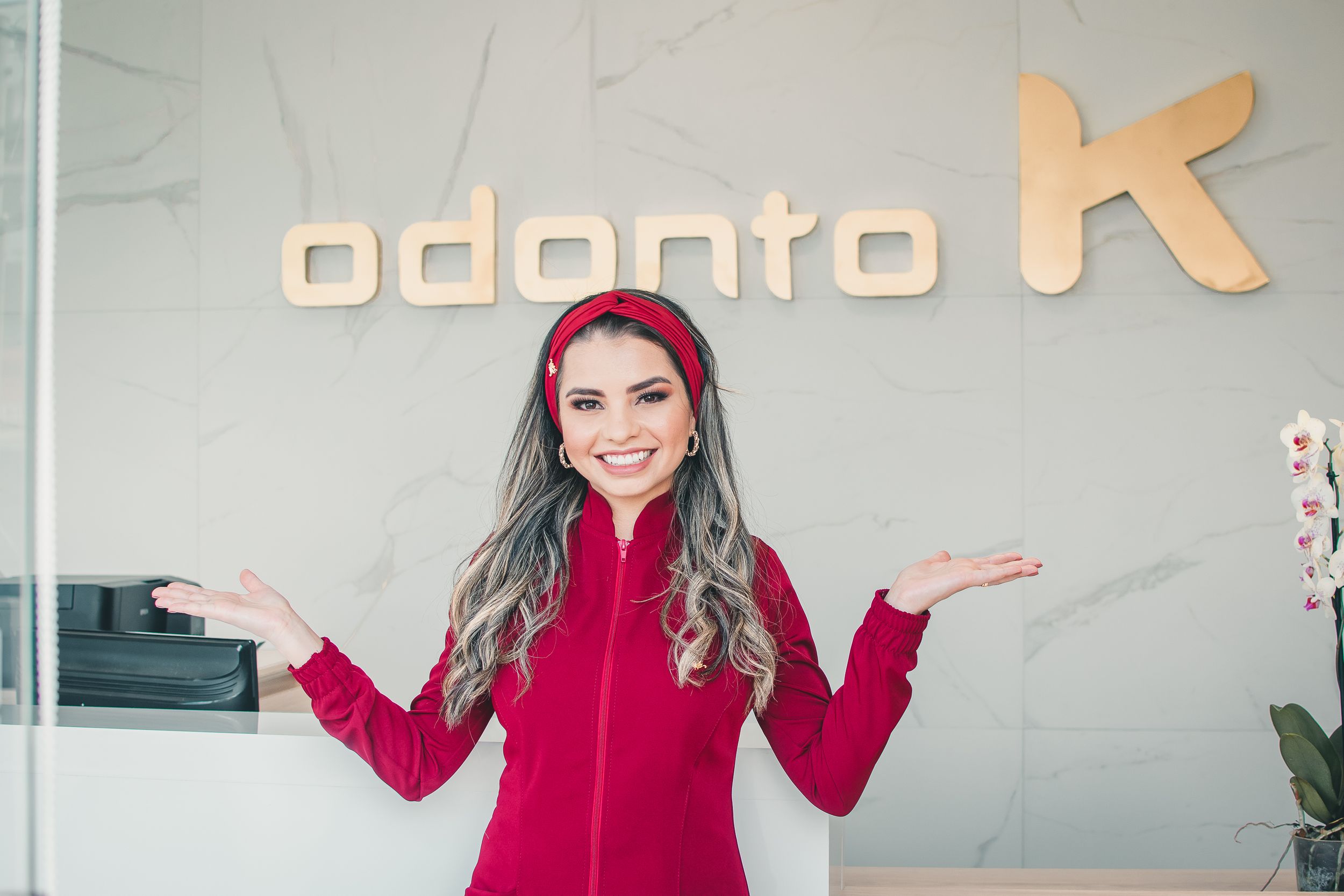 Healthcare provider in red uniform gesturing welcomingly under dental office sign.