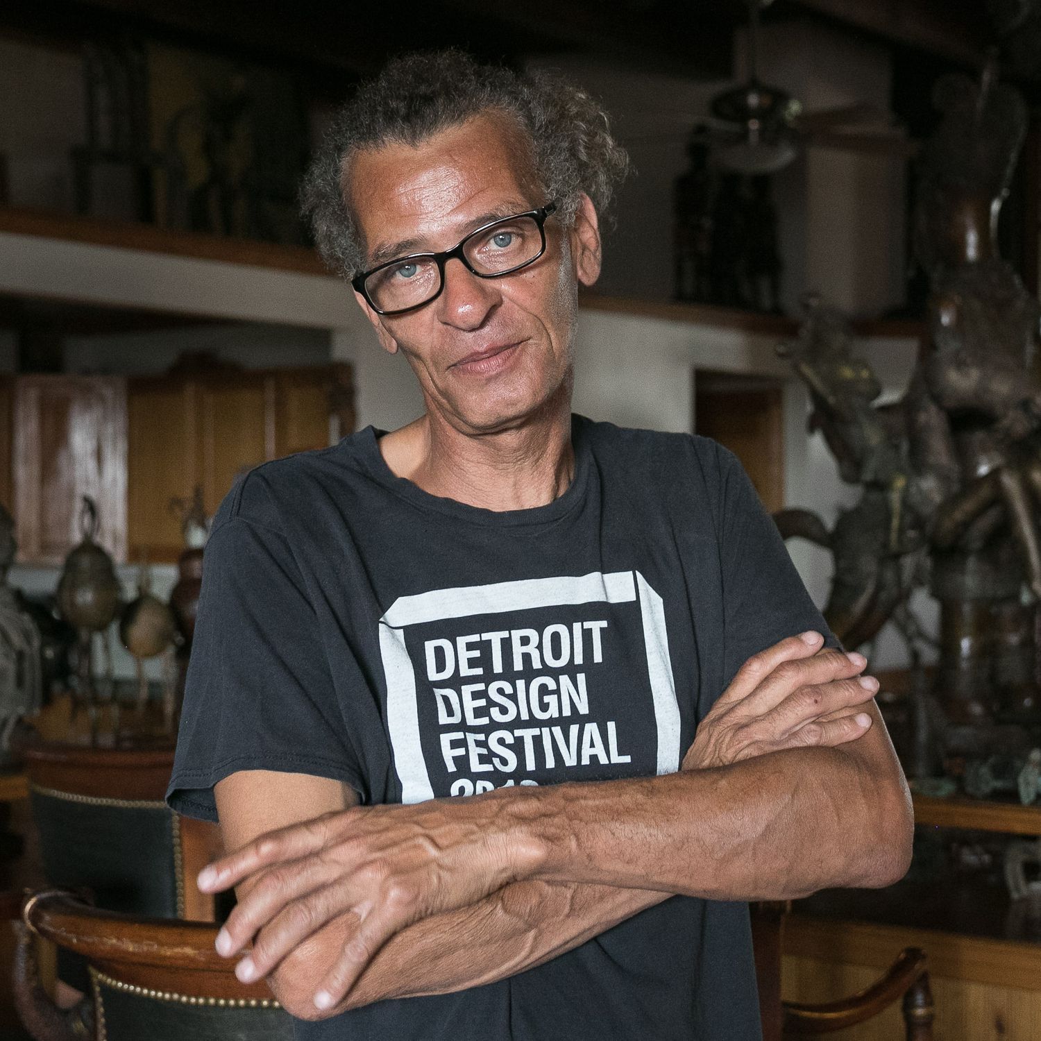 Artist crossing his arms in his work-live studio surrounded by sculptures.