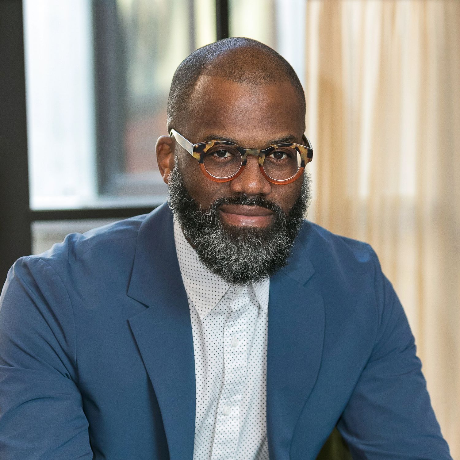 Portrait of a bearded black man in front of a window in the Detroit Shinola Hotel.
