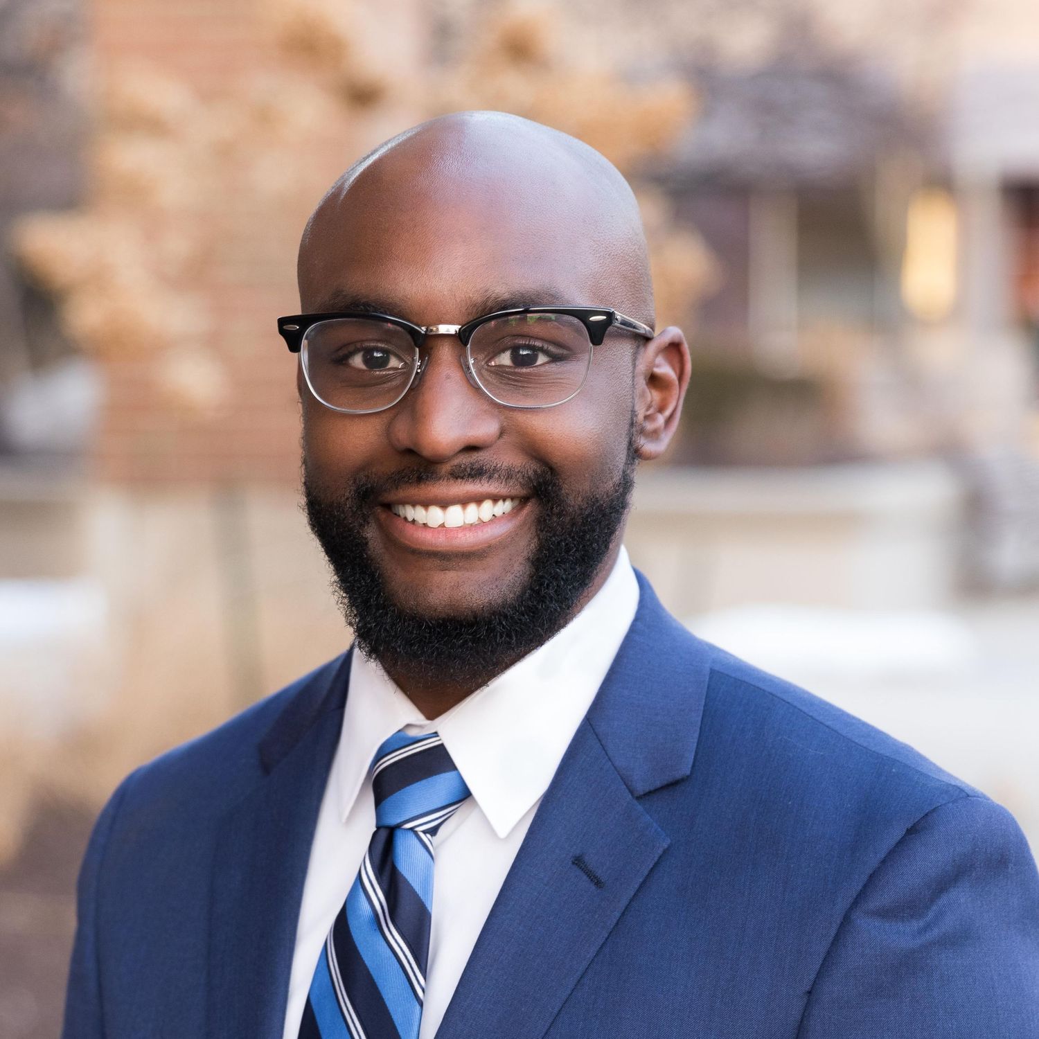 Headshot of a smiling black man in a business professional suit in an outdoor environment.