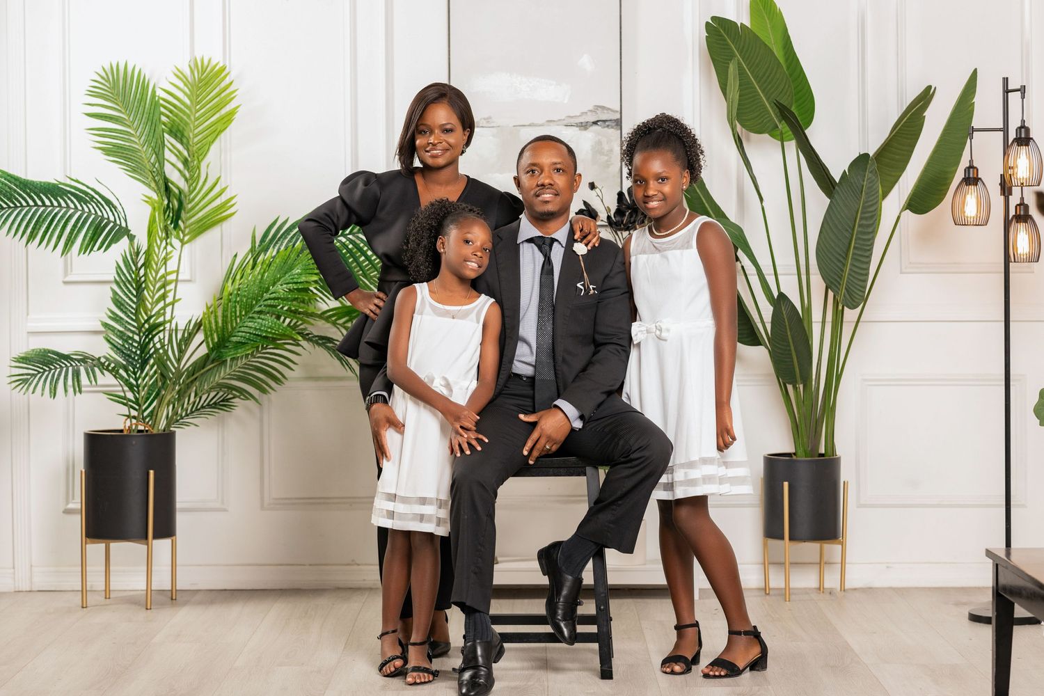 Family of four posing elegantly in white studio with tropical plants and modern gold accents.