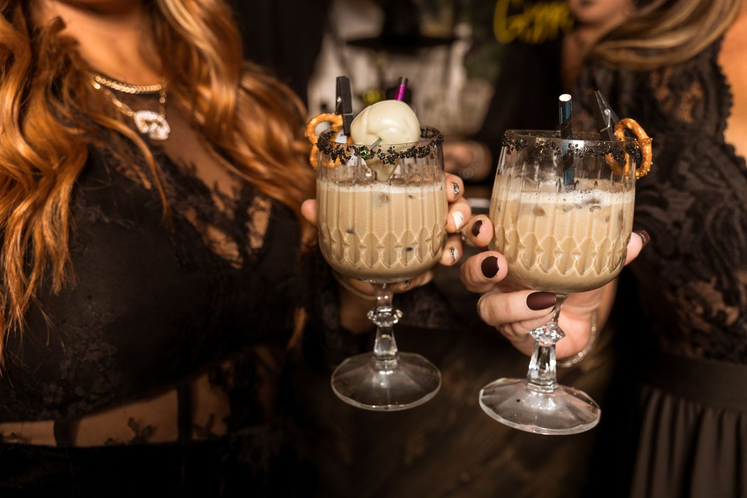 Two hands holding ornate Halloween cocktails garnished with spooky decorations.