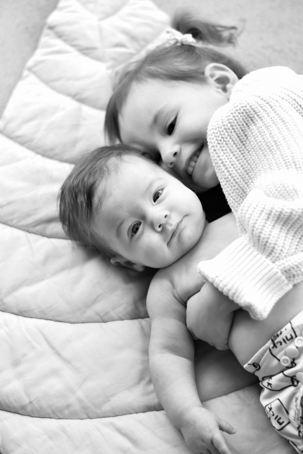 Two little ones sharing a tender moment while resting on white bedding.