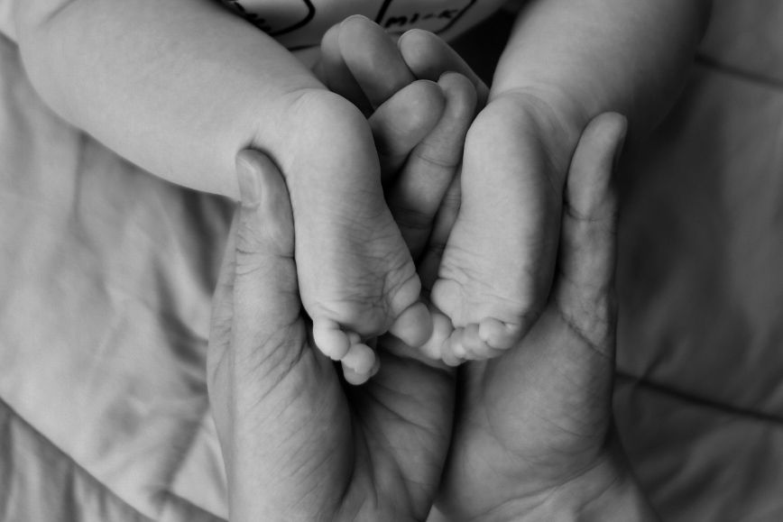 Close-up black and white photo of tiny feet being held in gentle hands.