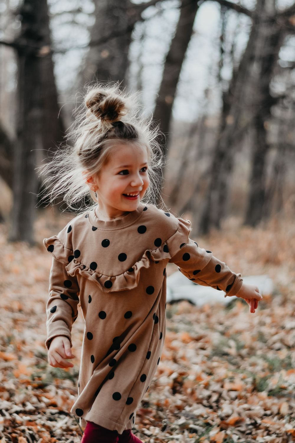 Joyful child in polka dot dress playing in autumn leaves.