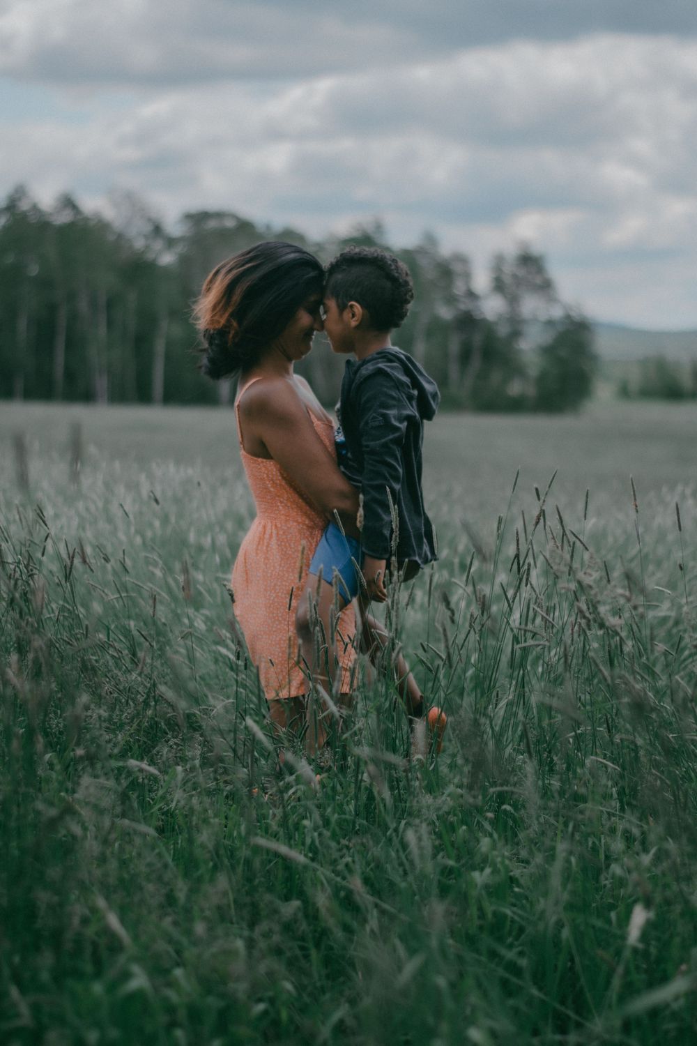 Couple embraces in tall grass field during cloudy afternoon.