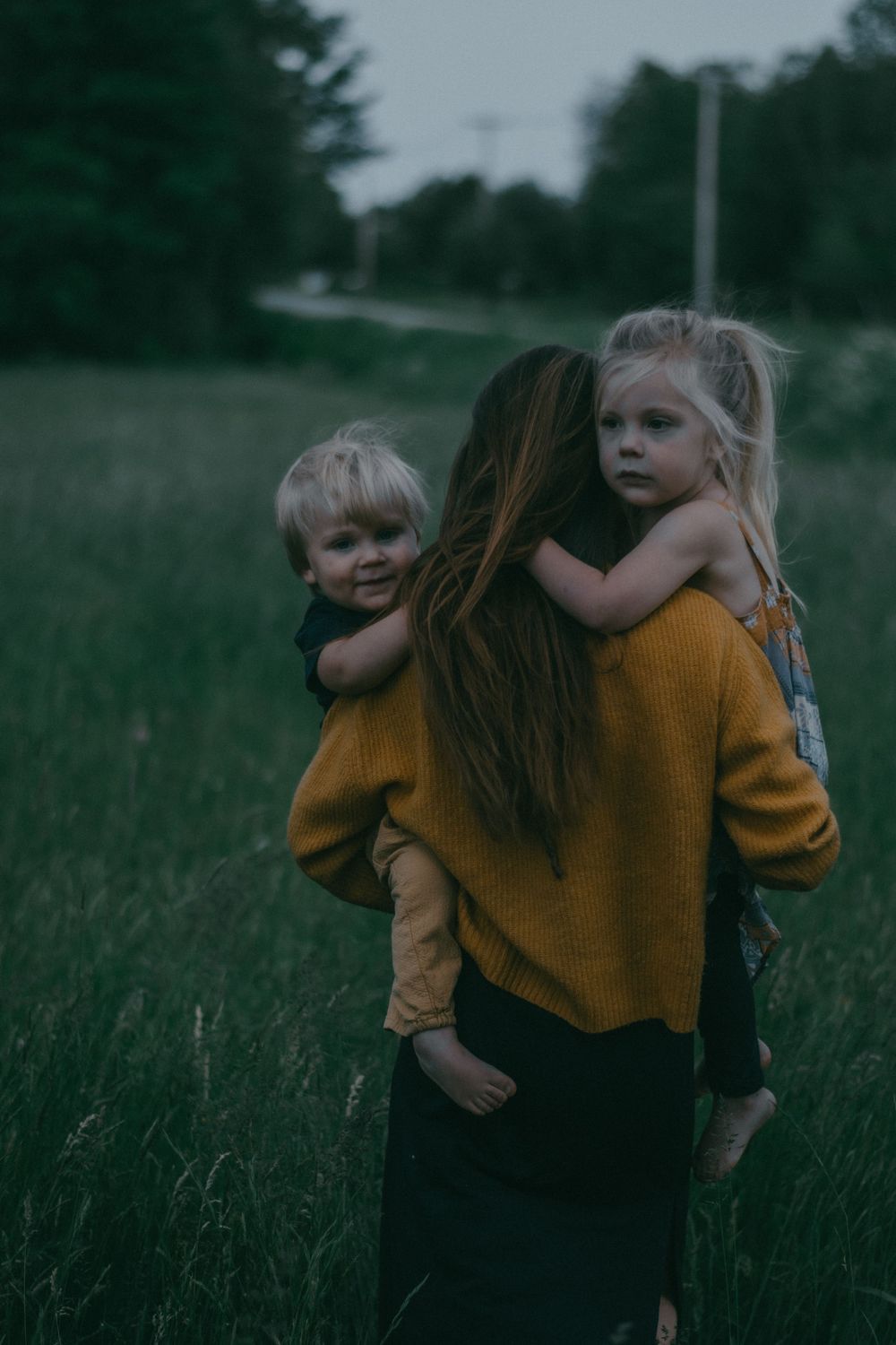 A gentle embrace in a mustard sweater against a dusky field backdrop.