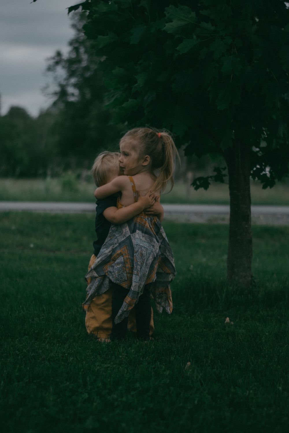 Two children share a tender embrace while playing outdoors on a moody overcast day.