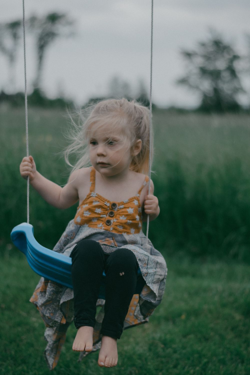 Young child enjoys swinging on a blue swing set in a grassy field.