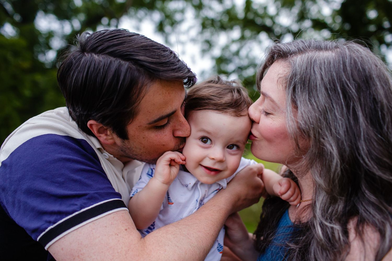 A tender family moment outdoors as parents shower love on their smiling baby.
