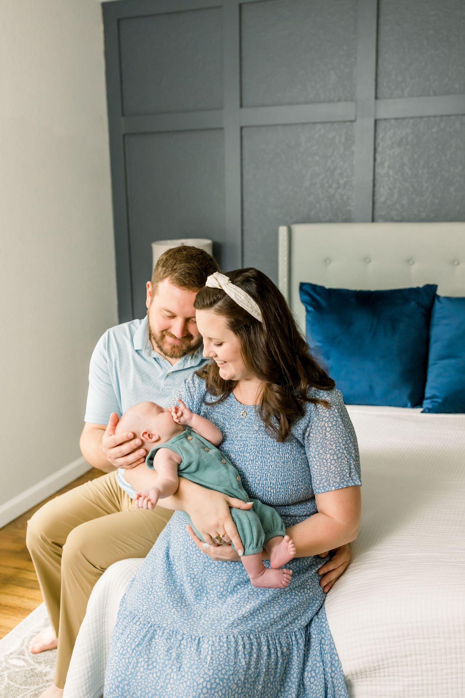 A tender family scene by a bed with sage green wall panels and hardwood floors.