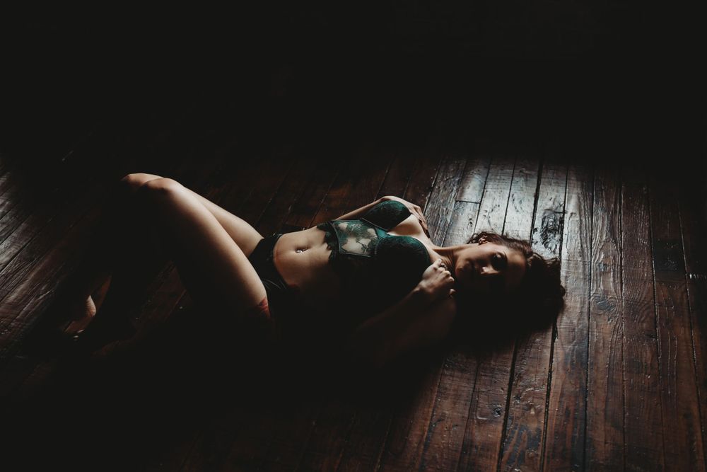 Dark wooden floor adds texture to intimate boudoir photography composition.