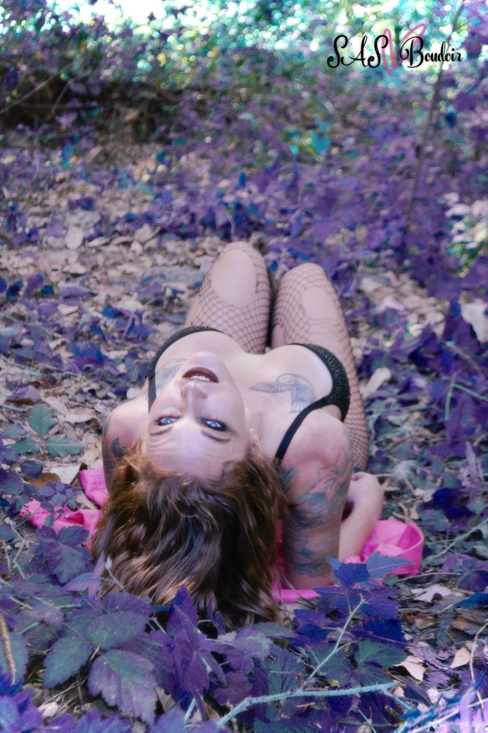 A person lies on autumn leaves with purple-tinted foliage creating a dreamy outdoor portrait scene.