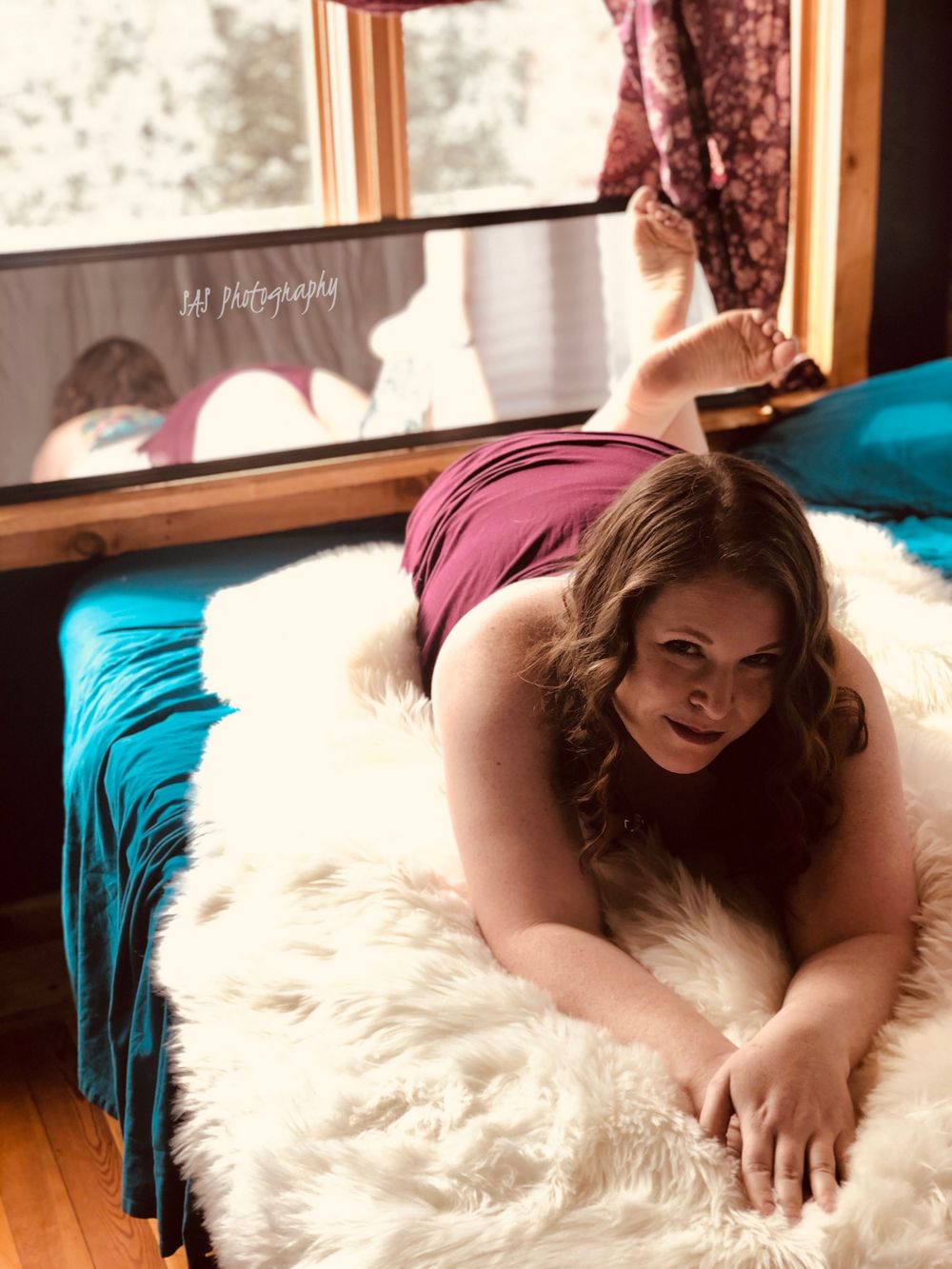 Intimate boudoir portrait on white fur rug with teal and burgundy tones.